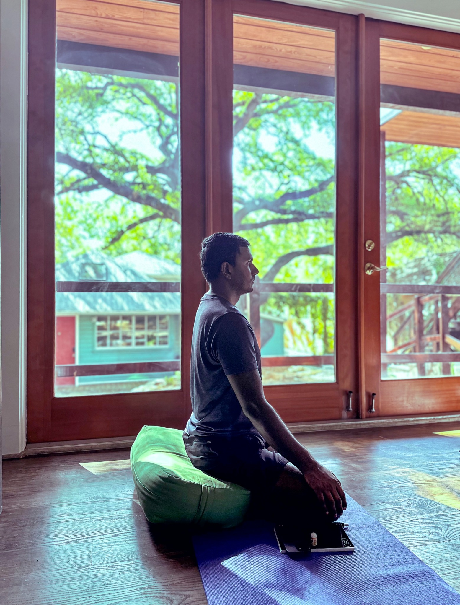 JJ Ruescas sitting on a cushion during a breathing practice beside large windows